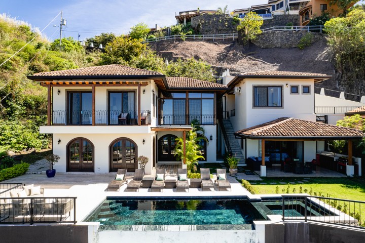 Two-story house with pool, sun loungers, and tiled roofs on a hillside.