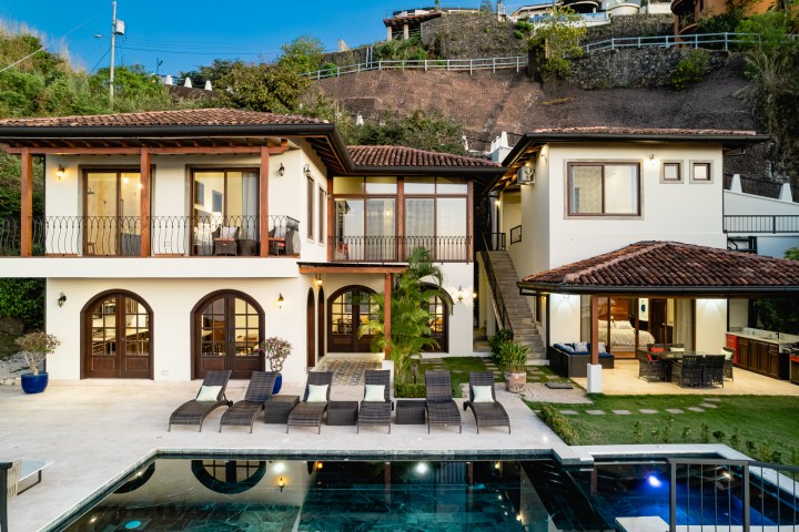 Modern villa with a pool, two-story design, and terracotta roof, set on a hillside with landscaped garden.