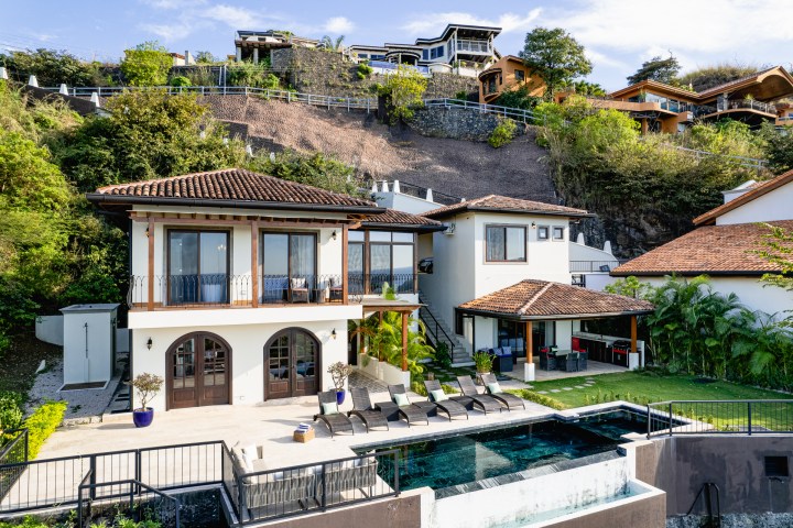 Modern hillside villa with pool, surrounded by lush greenery and multiple balconies.