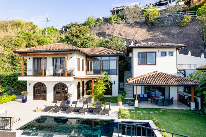 Luxurious villa with terracotta roof, pool, and outdoor seating area on a hillside.