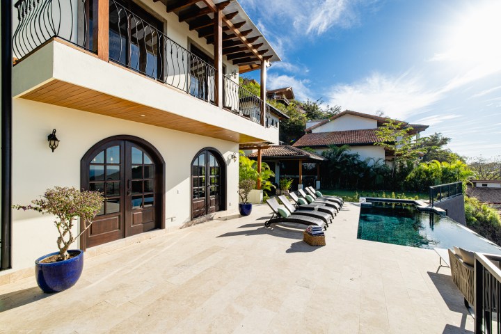 Luxury villa with pool, terrace, lounge chairs, and garden.