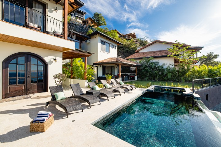 Modern villa with pool, sun loungers, and tropical garden under a blue sky.
