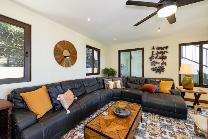 Modern living room with black sectional sofa, colorful pillows, ceiling fan, and decorative wall art.