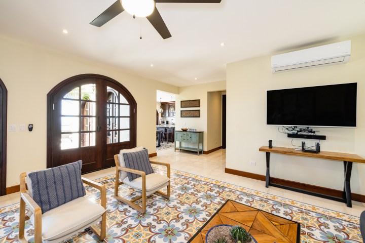 Modern living room with patterned floor tiles, two chairs, TV, and ceiling fan.