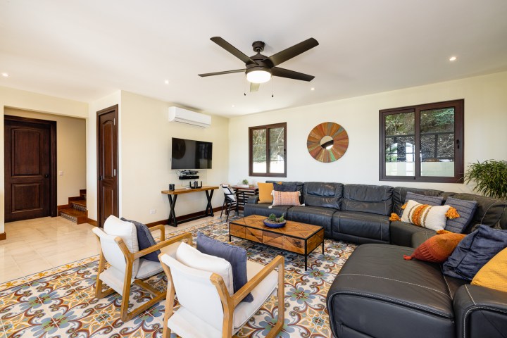 Spacious living room with a large black sectional sofa, patterned floor tiles, and wall-mounted TV.