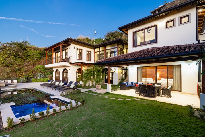 Modern two-story house with a pool and outdoor seating area at sunset.