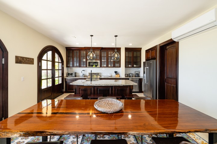 Modern kitchen with wooden cabinets, island, dining table, and double doors.