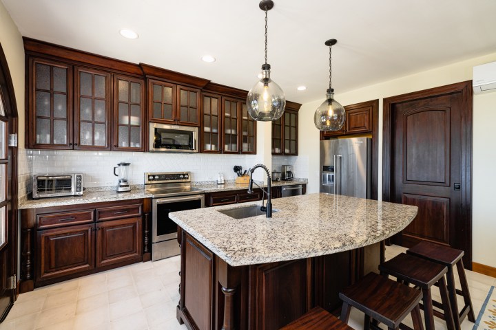 Modern kitchen with dark wood cabinets, large island, granite countertops, and pendant lights.