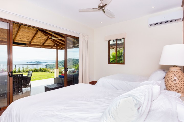 Bedroom with white beds and ocean view through sliding glass doors.
