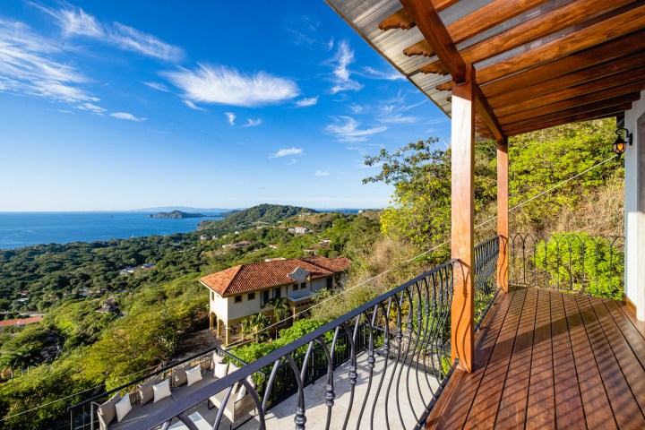 Wooden patio with ocean and hillside view under blue sky.