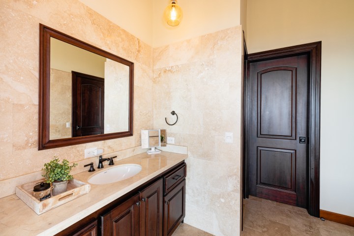 Bathroom with dark wood cabinets, a large mirror, and a sink against beige tiled walls.