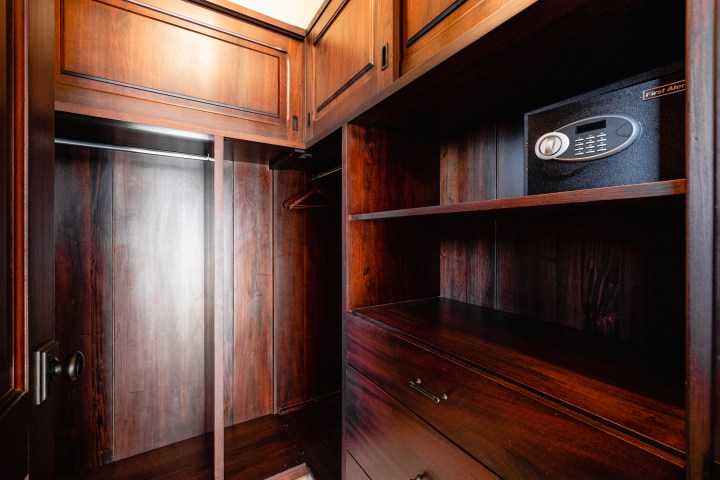 Wooden closet interior with shelves, empty hanging rod, and an electronic safe.