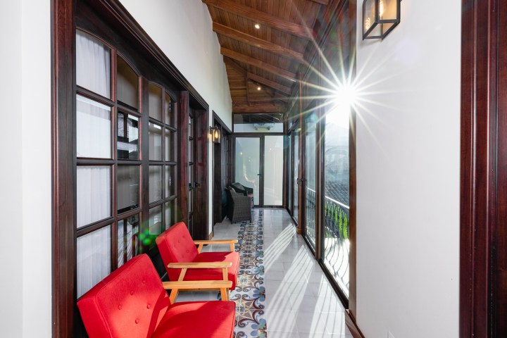 Bright hallway with red chairs, tile floor, wood ceiling, and sunlight streaming through large windows.