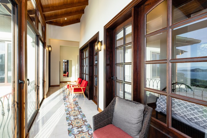 Bright hallway with wood-framed windows, red chairs, decorative floor tiles, and ocean view.