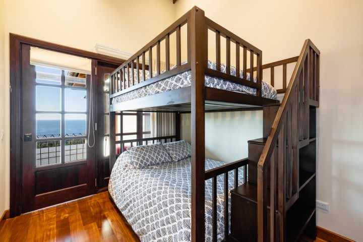 Room with wooden bunk bed, patterned bedding, and ocean view through glass door.