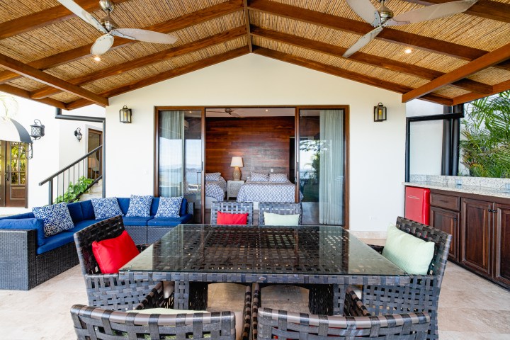 Patio with wicker furniture and ceiling fans, opening to a bedroom with sliding glass doors.