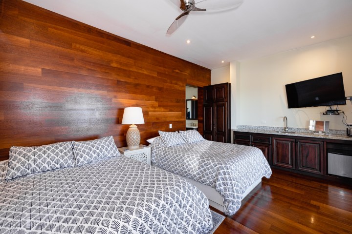 Modern bedroom with two beds, wood accent wall, and wall-mounted TV.