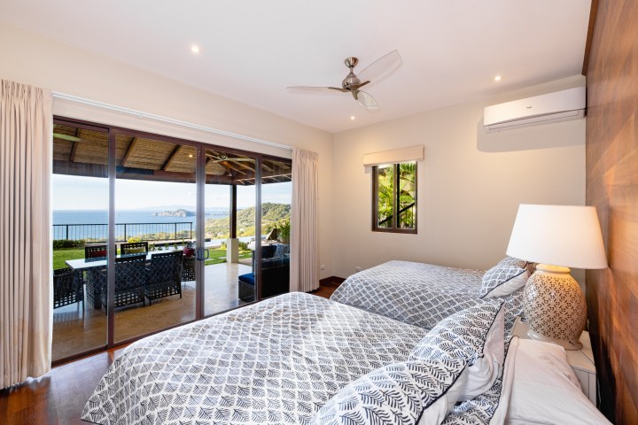 Bedroom with two beds, ocean view patio, and glass doors overlooking the sea.