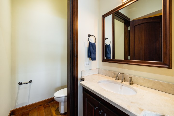Bathroom with a sink, mirror, towel, and toilet with wooden accents.