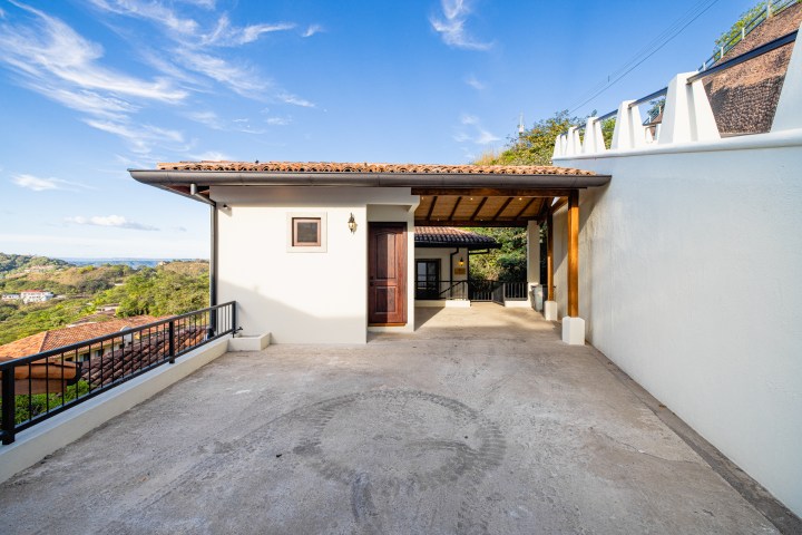 Driveway leading to a garage and house, with a scenic landscape and blue sky in the background.