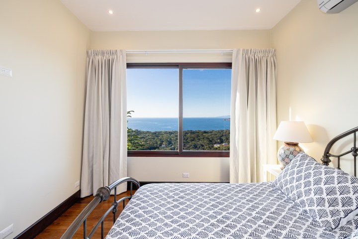 Bedroom with ocean view, white curtains, patterned bedspread, and a lamp on a side table.