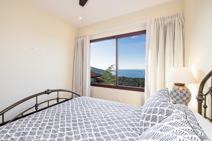 Bedroom with patterned bedding, ocean view through large window, and a lamp on nightstand.