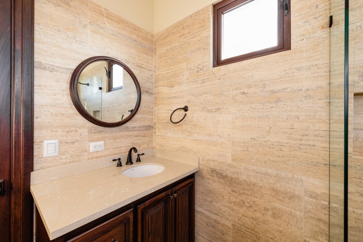Bathroom vanity with round mirror, sink, and beige wall tiles.