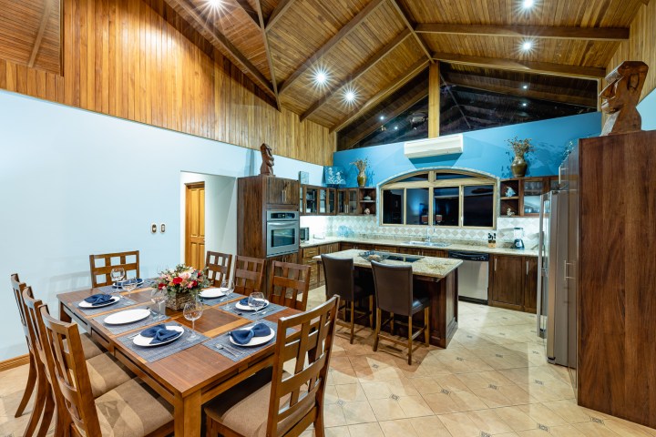 Spacious kitchen and dining area with wooden ceiling, table set for eight, and modern appliances.