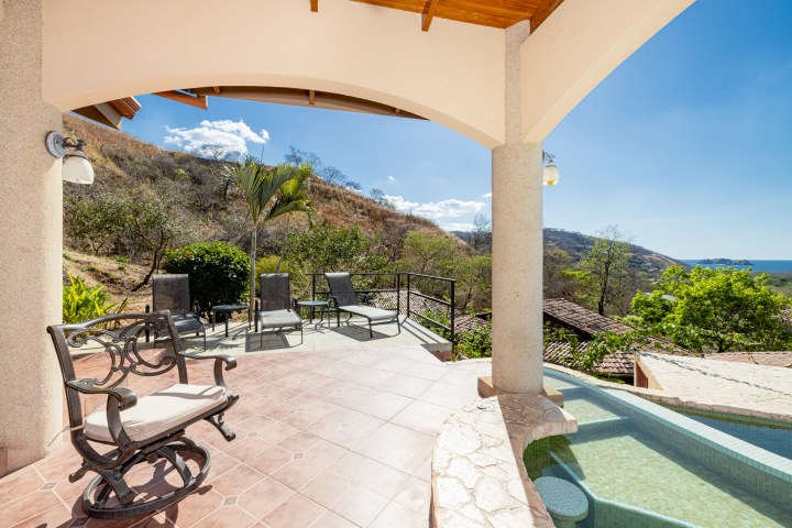 Sunny terrace with lounge chairs, a pool, and ocean view under a covered patio.