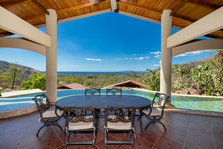 Outdoor patio with round table and chairs, overlooking infinity pool and ocean view.