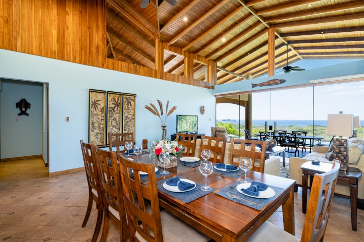 Spacious dining and living area with wooden ceiling, large windows, and ocean view.