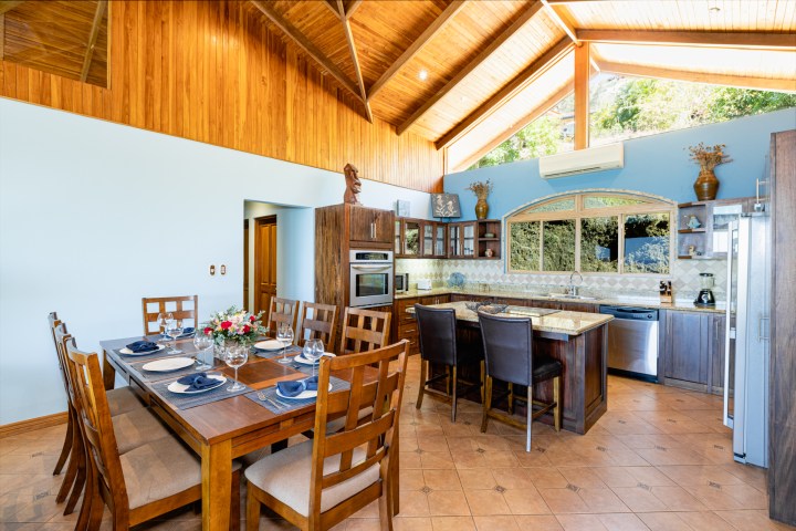 Spacious kitchen with wooden ceiling, dining table, island, and large windows offering outdoor views.