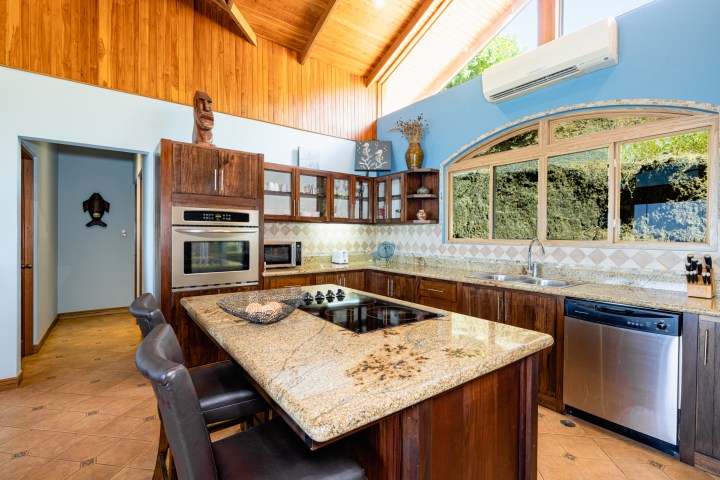 Modern kitchen with wood cabinets, granite countertops, and a large window, featuring an island and built-in appliances.