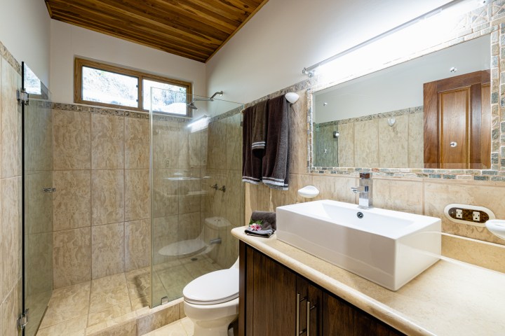 Modern bathroom with a glass shower, white sink, wooden accents, and beige tiles.