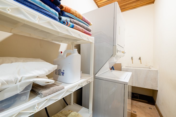 Laundry room with stacked washer-dryer, shelves of towels, and a sink.