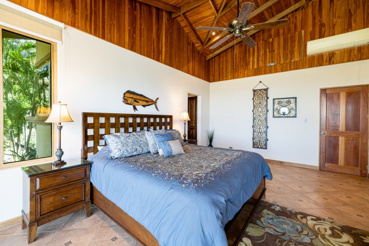 Cozy bedroom with wooden ceiling, large bed, lamps, and decorative wall art.