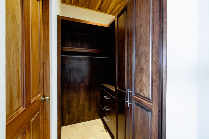 Wooden walk-in closet with cabinets and shelves, light tiled floor.