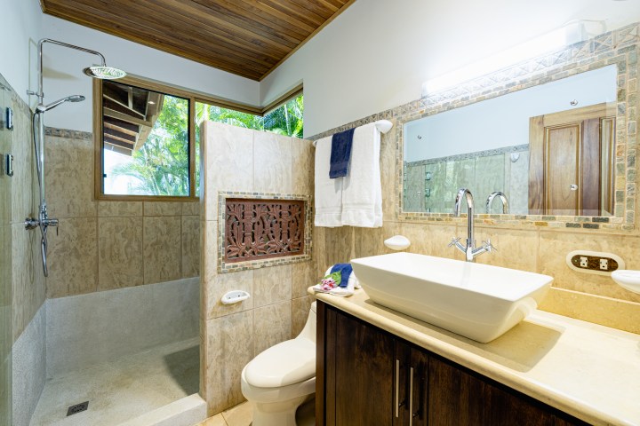 Bathroom with sink, mirror, shower, and towels. Natural light from window.