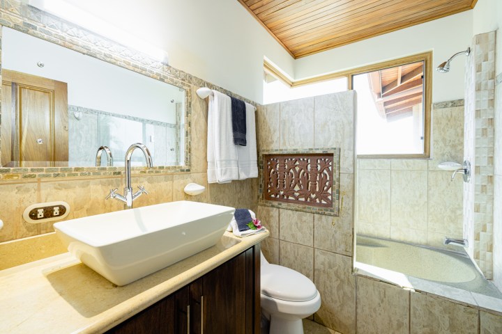 Modern bathroom with a stone sink, mirror, toilet, and natural light from a window.