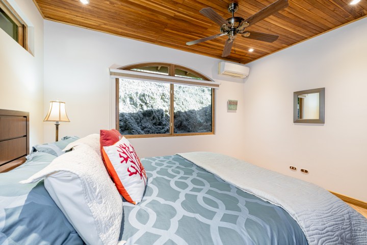Bedroom with wooden ceiling, large bed, window with mountain view, and ceiling fan.
