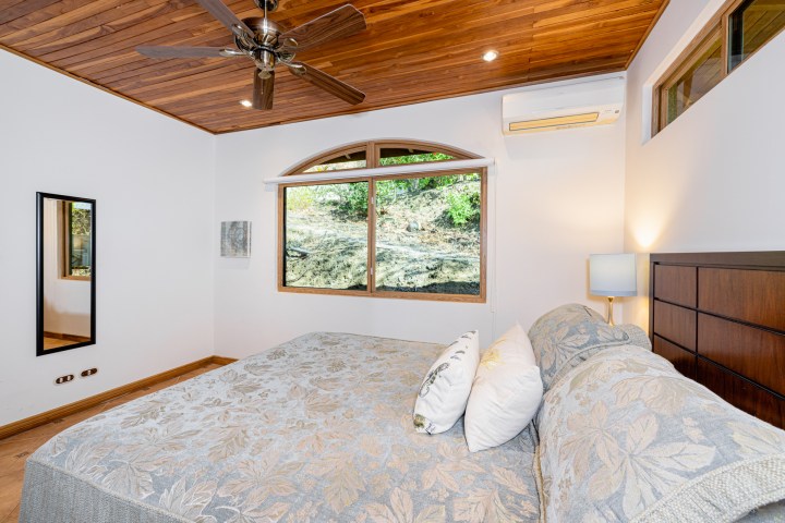 Bedroom with a large bed, wooden ceiling, window with a view, and air conditioner on the wall.