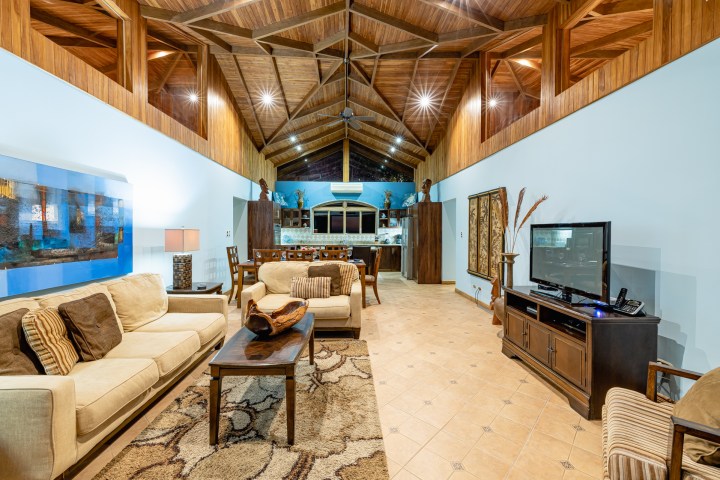 Spacious living room with wooden ceiling, beige couches, TV, and dining area.