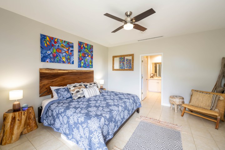 Bedroom with blue bedding, ceiling fan, and colorful wall art.
