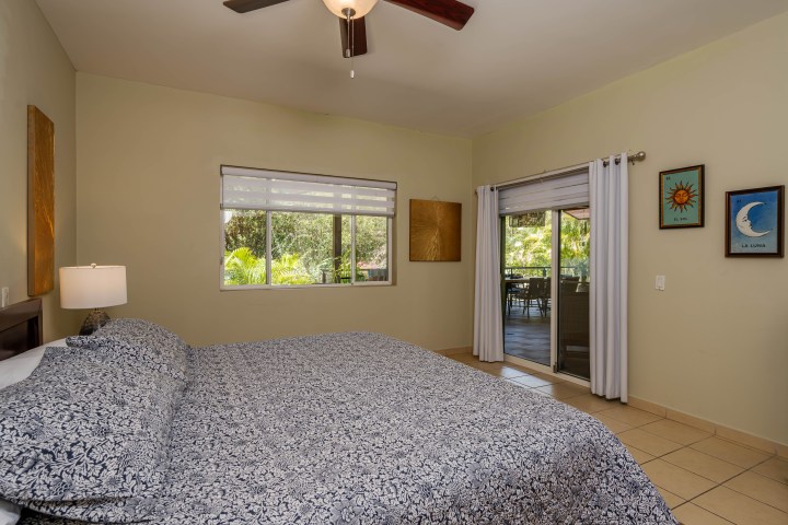 Bedroom with patterned bedspread, ceiling fan, window, and sliding door leading to outdoor patio.