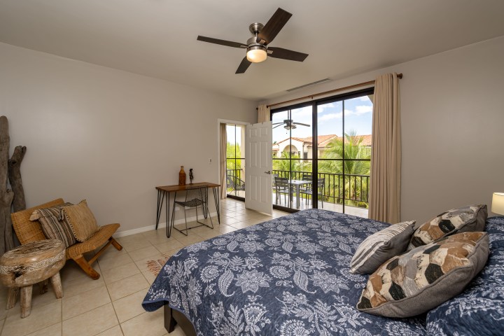 Bedroom with blue bedspread, balcony view, ceiling fan, and rustic furniture.