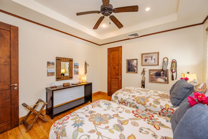Bedroom with two beds, floral bedding, wooden furniture, ceiling fan, and wall art.