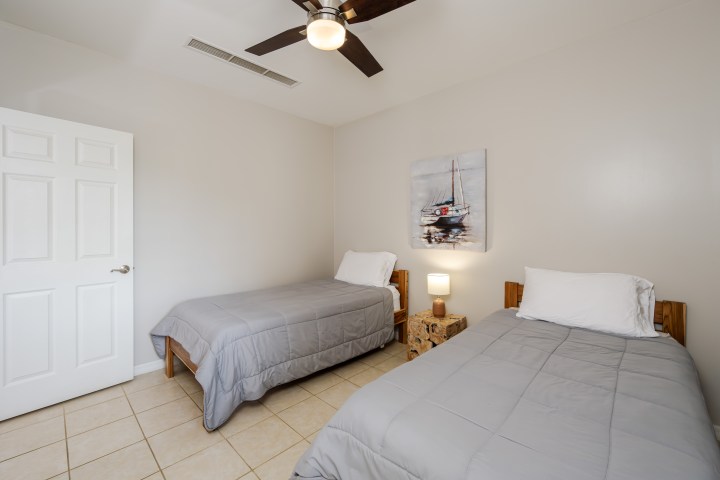 Two beds in a room with a ceiling fan and nautical artwork.