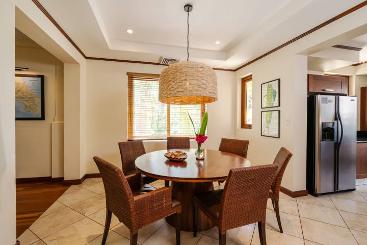 Dining area with round table, wicker chairs, pendant light, and stainless fridge in corner.