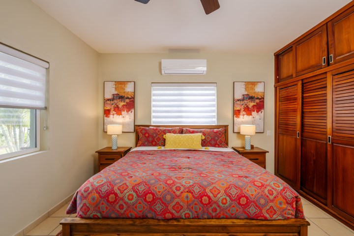 Bedroom with patterned red bedding, two lamps, and abstract art above a wooden bed, window on the left.