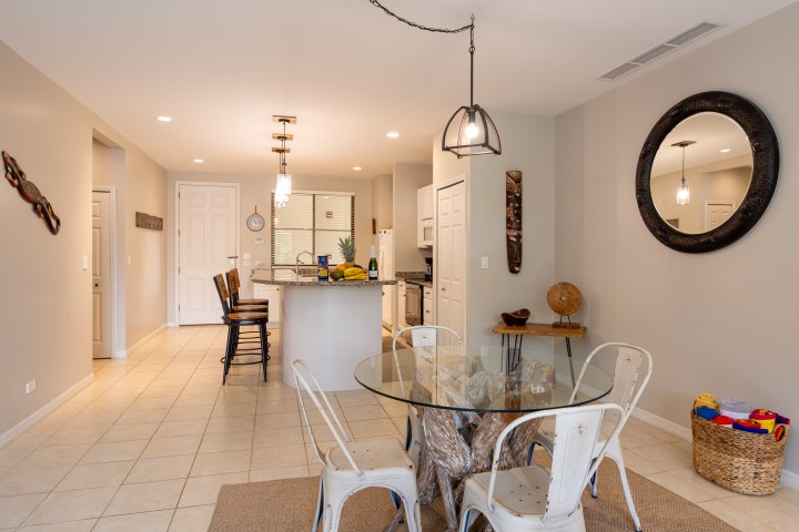 Modern kitchen and dining area with glass table, metal chairs, and hanging lights.